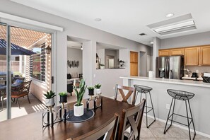 A modern kitchen with a dining area, featuring a wooden table, bar stools, and a kitchen island.