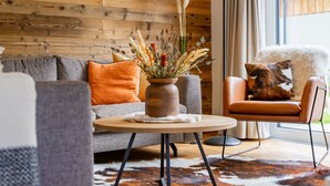 A cozy living room with a wooden wall, a round table, a sofa, a chair, and a large window. - Detached luxury chalet (Kreischberg)
