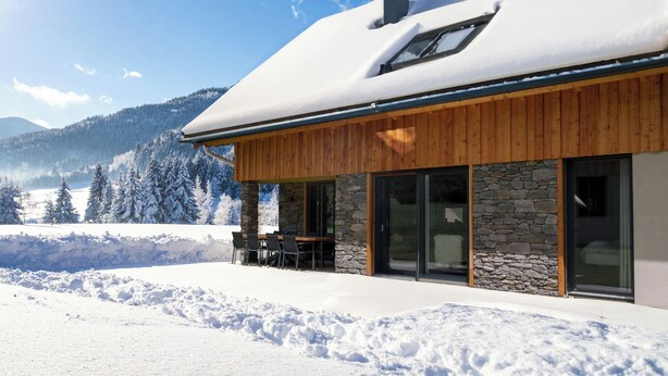 A modern house with a stone facade, large windows, and a covered patio with outdoor seating. - Detached luxury chalet (Kreischberg)
