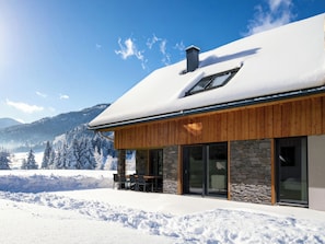 Une maison moderne avec une façade en pierre, de grandes fenêtres et un patio couvert avec un espace salon extérieur.