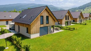 A row of wooden cabins with sloped roofs, set in a grassy area with mountains in the background. - Detached luxury chalet (Kreischberg)