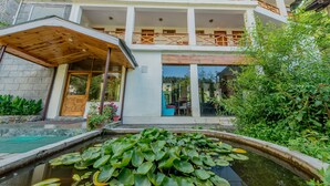 Un edifici de diverses plantes amb entrada coberta, una piscina plena de nenúfars i vegetació abundant.