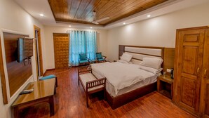 Habitació d'hotel amb sostre de fusta, un llit gran, una televisió, escriptori i finestra amb cortines.