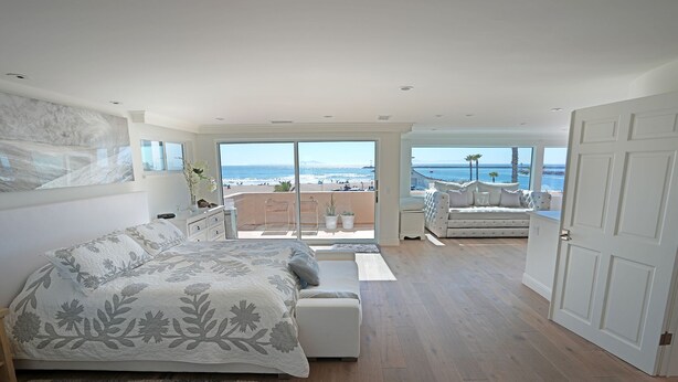 Un dormitorio con una cama grande, un balcón con vistas a la playa y una zona de estar con vistas al océano.