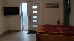 Una habitación con una mesa de comedor de madera, un televisor de pantalla plana montado en la pared, una puerta con paneles de vidrio esmerilado y un letrero que dice 'HOME' en la pared.