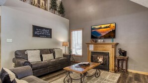 Ein Wohnzimmer mit Kamin, einer Couch, einem Couchtisch und einem an der Wand befestigten Fernseher.
