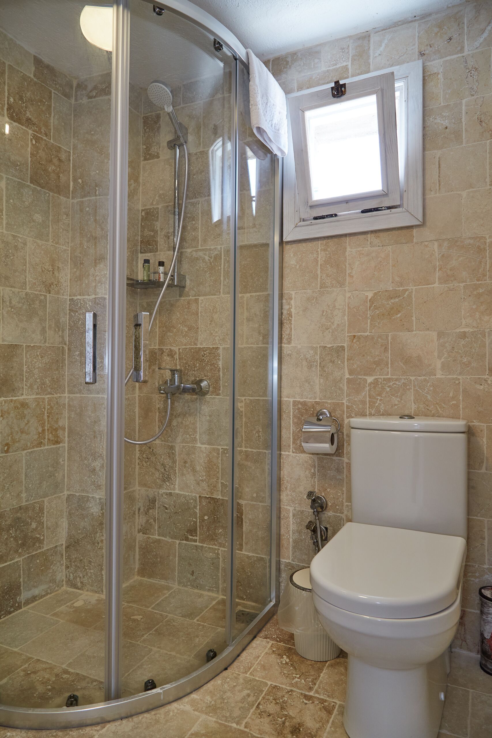 A bathroom with a glass-enclosed shower, a toilet, and a small window.