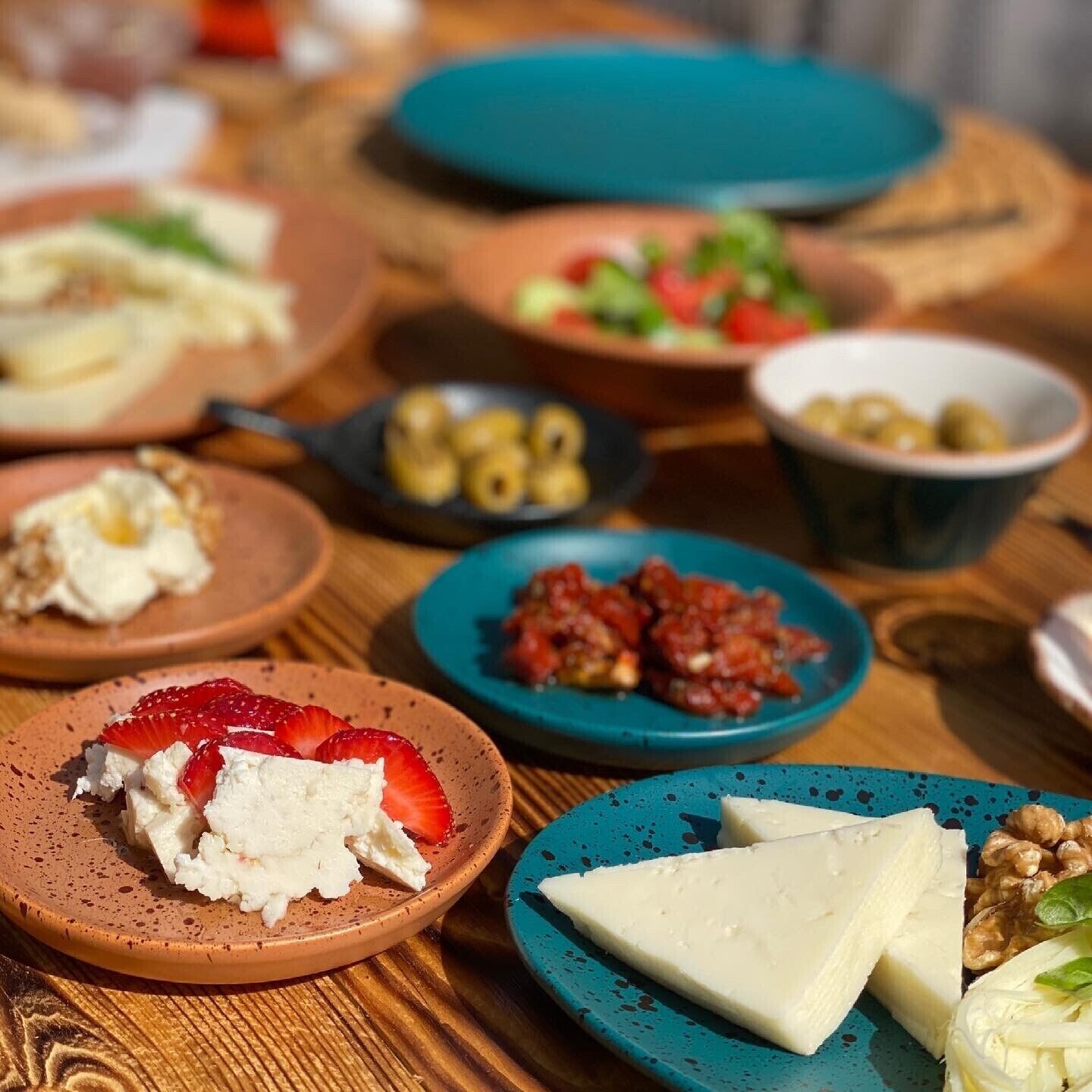 Une table en bois sur laquelle on trouve divers aliments, notamment du fromage, des fraises, des olives et des noix.