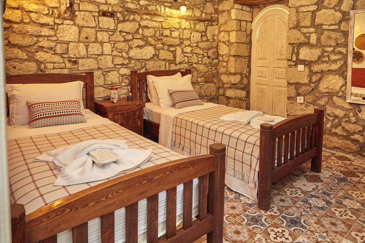 A room with three wooden beds, stone walls, and a tiled floor.