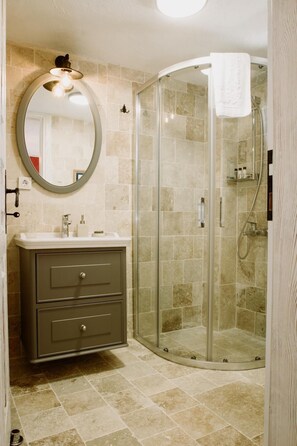 A bathroom with a glass-enclosed shower, a vanity with a mirror, and beige tiles. - Morisi Avlu (Cesme)
