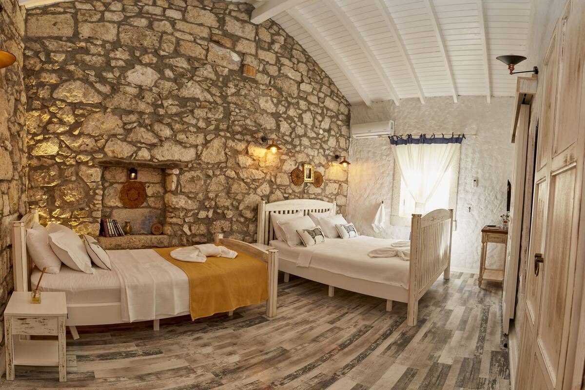 A bedroom with two beds, stone walls, wooden flooring, and a stone fireplace.