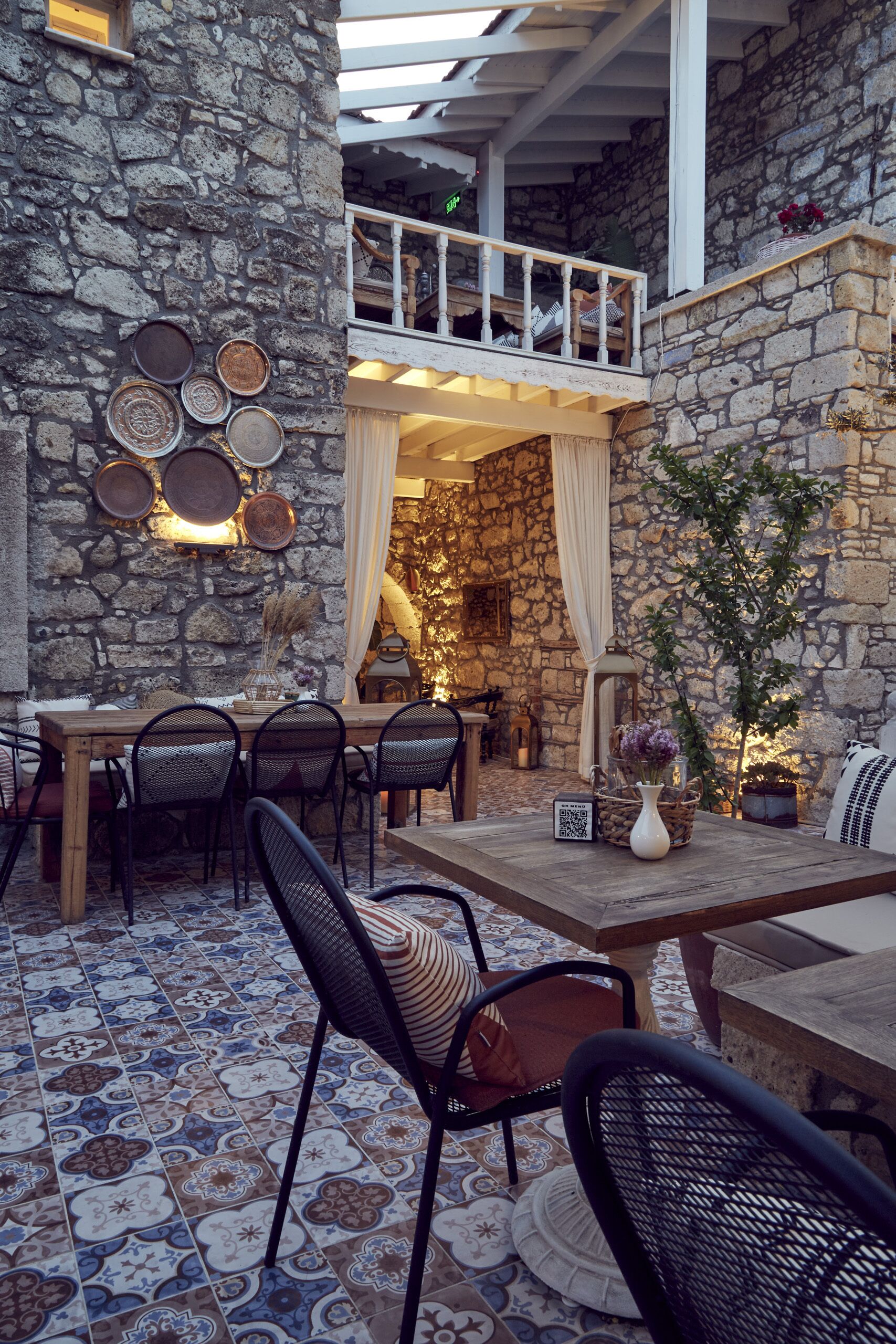Un patio con paredes de piedra, una mesa y sillas de madera, un farol colgante y vistas al interior.