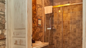 Un bany rústic amb paret de pedra, porta de fusta, un lavabo amb mirall, vàter i dutxa.