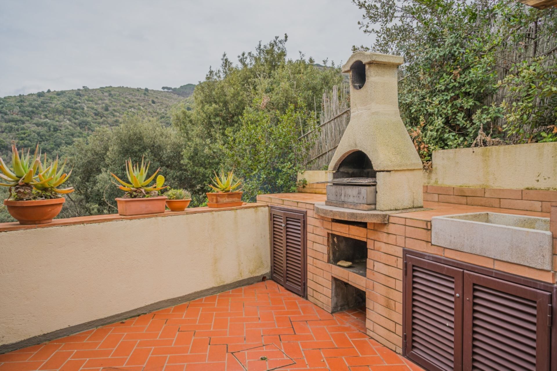 An outdoor patio with a brick floor, a stone oven, and potted plants.