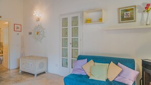 A room with a blue sofa, a white cabinet, a door with glass panels, and a wall-mounted shelf with yellow containers.