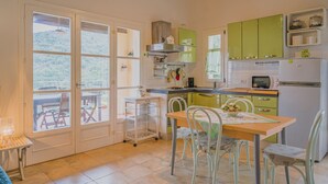 A kitchen with a dining area, featuring a table with chairs, a microwave, a refrigerator, and a view through the doors.