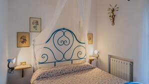 A bedroom with a bed, a bedside table with a lamp, a radiator, and wall-mounted pictures. - APP.TI STRACCOLIGNO - CASA MIMMA (Capoliveri)