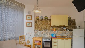 A compact kitchen with a stove, oven, and a small dining area with a table and chairs. - APP.TI STRACCOLIGNO - CASA MIMMA (Capoliveri)