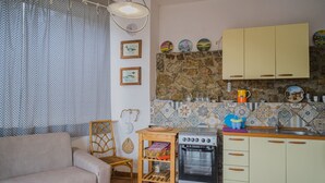 A compact living space with a sofa, a dining table, a small kitchen area with a stove, and a stone wall backsplash. - APP.TI STRACCOLIGNO - CASA MIMMA (Capoliveri)