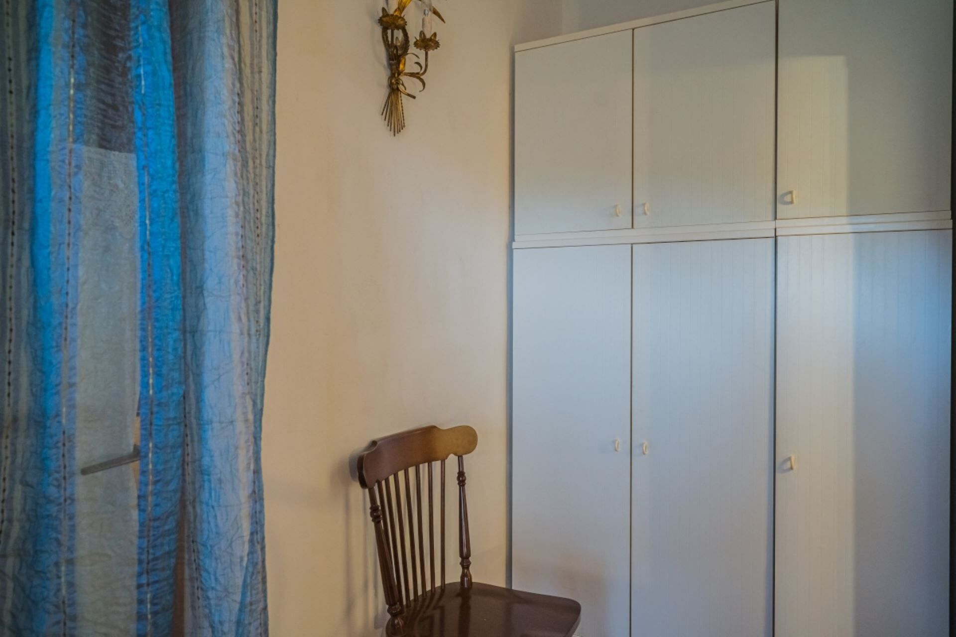 Una habitación con una silla de madera, un armario y una cortina.