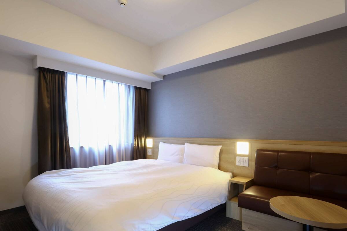 Habitación de hotel con una cama grande, una mesita redonda y un banco de cuero marrón.