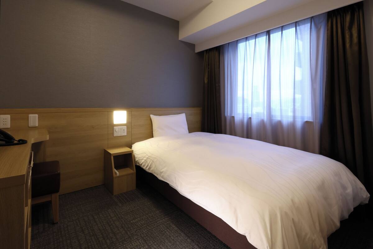 Una habitación de hotel con cama, mesita de noche, lámpara y teléfono.