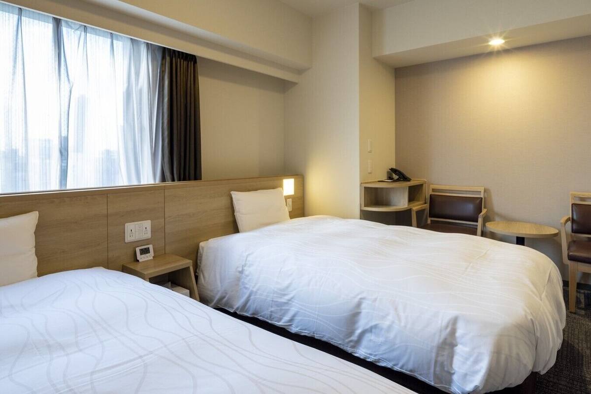 Una habitación de hotel con dos camas, un escritorio, una silla y una mesita.