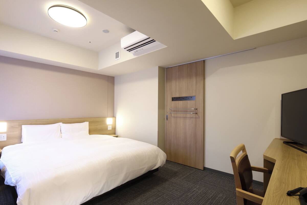 Una habitación de hotel con cama, escritorio con silla, televisión y armario.