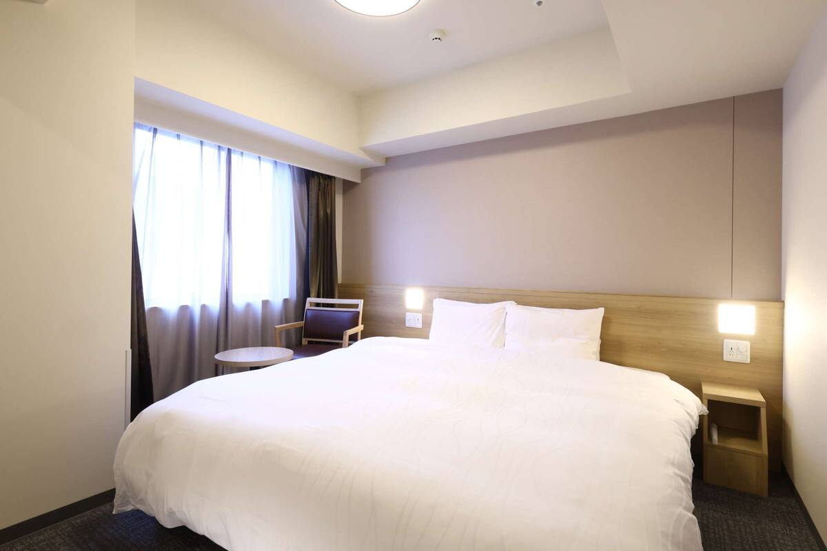 Una habitación de hotel con una cama grande, una mesita redonda, una silla y una mesita de noche.