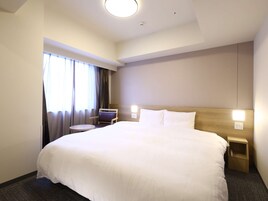 Ein Hotelzimmer mit einem großen Bett, einem kleinen runden Tisch, einem Sessel und einem Nachttisch.