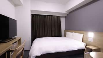 Habitación de hotel con cama, televisor sobre un mueble de madera, mesita de noche y lámpara fijada a la pared.