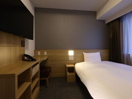 Habitación de hotel con cama, escritorio con teléfono, silla, mesita de noche y televisor montado en la pared.