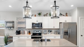 Une cuisine moderne dotée d’un îlot central, d’appareils électroménagers en acier inoxydable et d’éléments décoratifs fixés au mur.