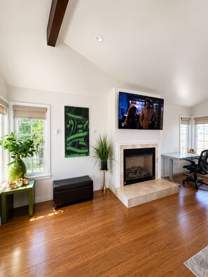 A living room with a fireplace, a television mounted above it, and a large green abstract painting on the wall.