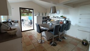 A modern kitchen with a dining area, featuring a large island, black chairs, and a hanging light fixture. - Magnificent, peaceful villa surrounded by olive trees. Exceptional panoramic view (Fayence)