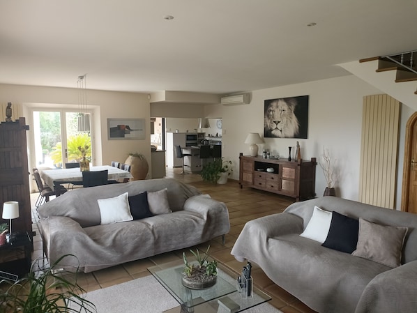 A spacious living room with two grey sofas, a glass coffee table, and a dining area with a table and chairs.
