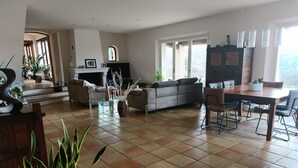 A spacious living room with a fireplace, a dining area, and a view of the outdoors. - Magnificent, peaceful villa surrounded by olive trees. Exceptional panoramic view (Fayence)