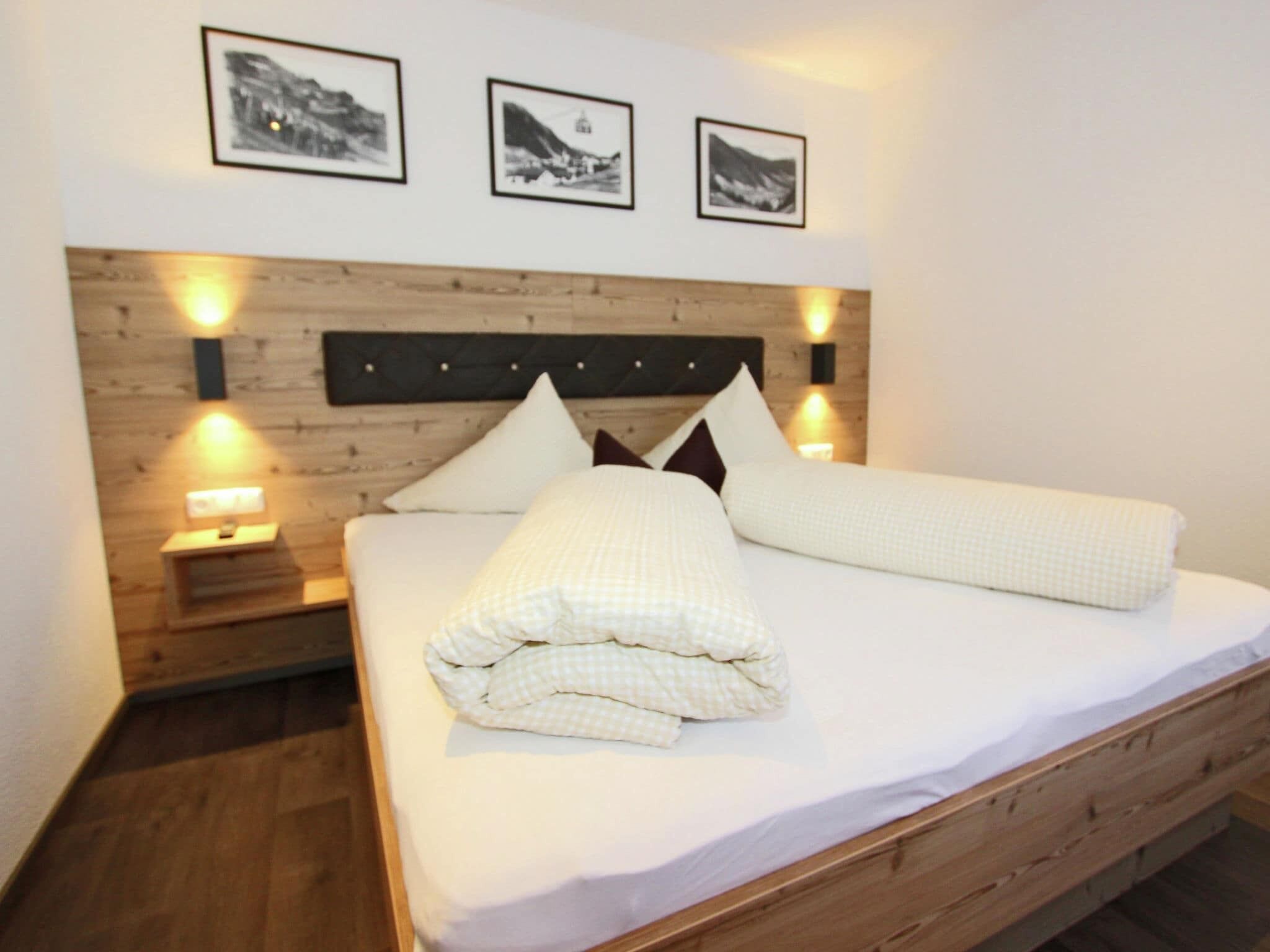 Een net opgemaakt bed met een geruit plaid, een houten hoofdbord en drie ingelijste foto's aan de muur erboven.
