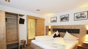 A modern bedroom with a wooden bed, a walk-in closet, a shower, and framed pictures on the wall. - Apartment in See near Ski Slopes (See)