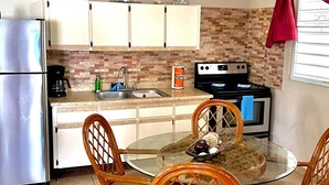 A compact kitchen with a refrigerator, stove, and dining area with wicker chairs. - Beautiful, spacious house 9 minute drive to beach with electric generator (Rincón)