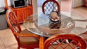 A dining area with a round glass table, wooden chairs, a microwave, and a cabinet with kitchenware. - Beautiful, spacious house 9 minute drive to beach with electric generator (Rincón)