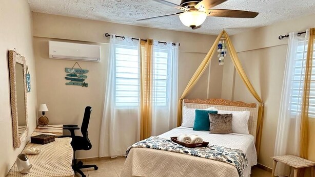 A bedroom with a bed, a desk, a chair, a ceiling fan, and curtains. - Beautiful, spacious house 9 minute drive to beach with electric generator (Rincón)