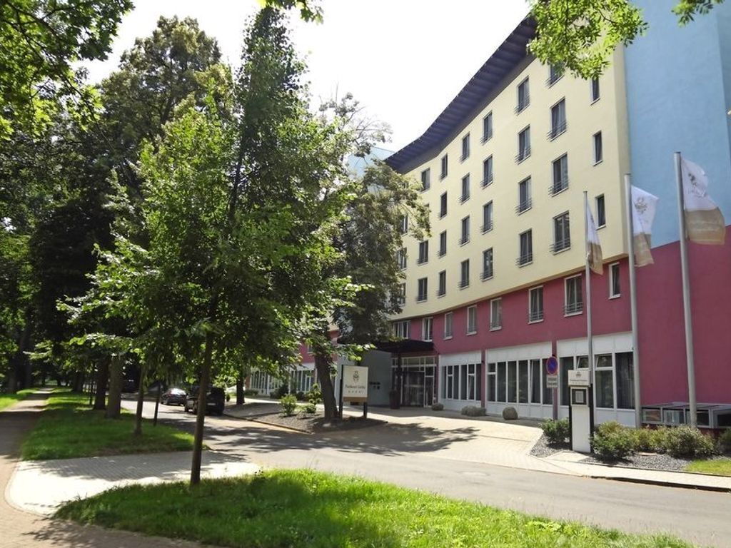 Un hôtel à plusieurs étages, doté d’une façade rouge et beige, d’une entrée couverte et d’un parking aménagé avec des arbres.