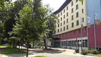 Un hôtel à plusieurs étages, doté d’une façade rouge et beige, d’une entrée couverte et d’un parking aménagé avec des arbres.
