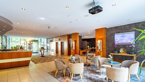 A modern hotel lobby with a reception desk, seating area, and a large screen displaying information. - Parkhotel DZ Standard - Parkhotel Görlitzs (Görlitz)