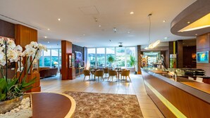 A modern hotel lobby with a reception desk, seating area, and large windows offering a view of the outdoors. - Parkhotel DZ Standard - Parkhotel Görlitzs (Görlitz)