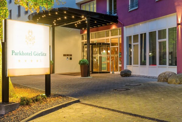 The exterior of Parkhotel Görlitz with a signboard, entrance, and a covered area with lights.