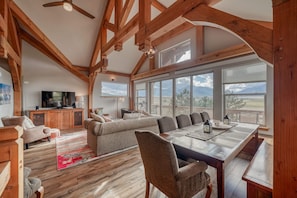 A spacious living area with a large wooden dining table, comfortable seating, and a television in the background.