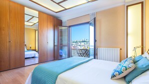 A bedroom with a large bed, a view of the city through an open door, and a balcony with a table and chairs. - Cagliari Upper House (Cagliari)