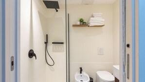 Ein modernes Badezimmer mit Glasabtrennung, einer Dusche, einer Toilette und einem kleinen Ablagebereich mit Handtüchern.